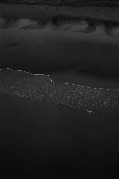 A thin line of sea foam on wet dark sand